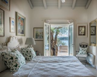 A bedroom at a Corfu villa with green patterned cushions, framed art on all walls, and a sea view through French windows