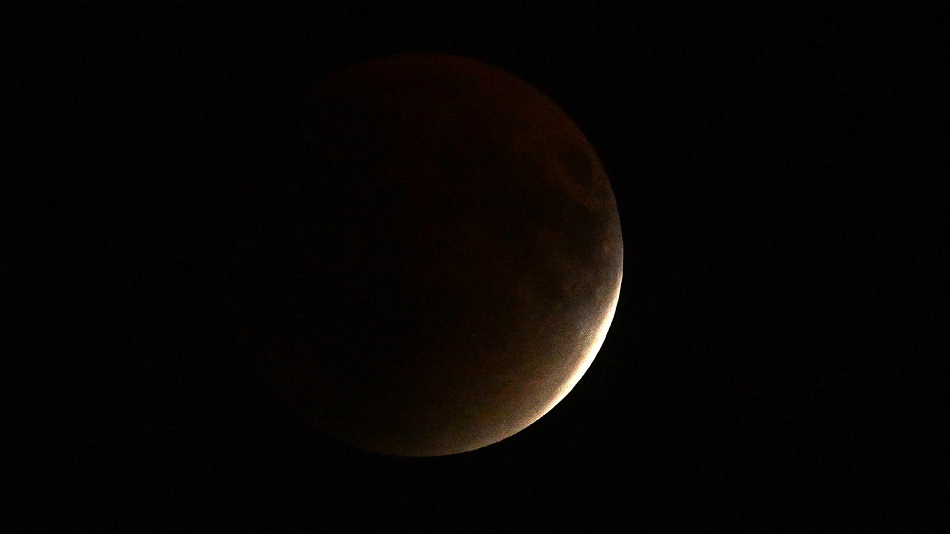 The moon is shown against a black sky. A thin crescent on its right edge is lit by bright sunlight and the rest is bathed in shadow.