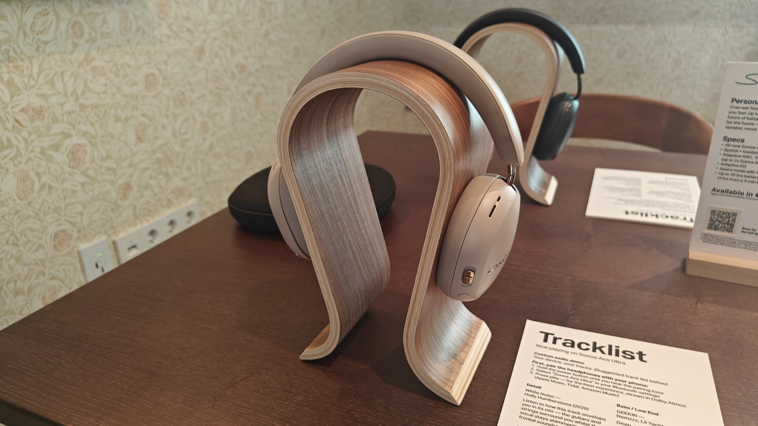 Sand coloured Sonos Ace Ultra headphones on a brown headstand.