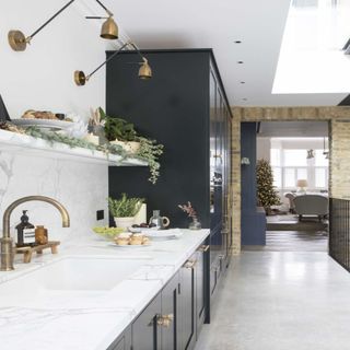 white marble countertops with brass lights and taps, black cabinets and exposed brick wall