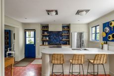 A kitchen with a blue tiles backsplash, a terracotta tiled floor, and rattan stools at a white island