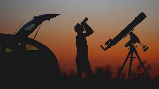 Check out our best binoculars for stargazing. Here a man is standing behind his car using a pair of binoculars to look at the stars. 