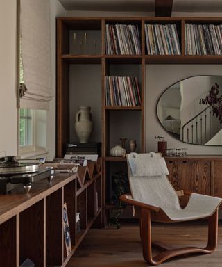 A lounge space with a wooden and boucle chair, a record player, and built-in wooden shelves storing records and decor