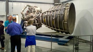 A California Science Center guide discusses the Space Shuttle Main Engine display with invited guests.