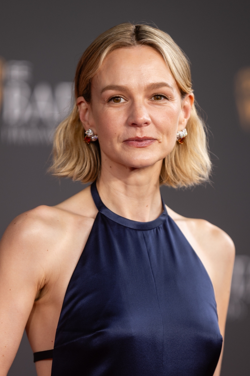 Carey Mulligan is pictured with a wavy bob, with the front strands tucked behind her ears, and wearing a navy Prada dress at the 2026 EE BAFTA Film Awards at The Royal Festival Hall on February 22, 2026 in London, England.