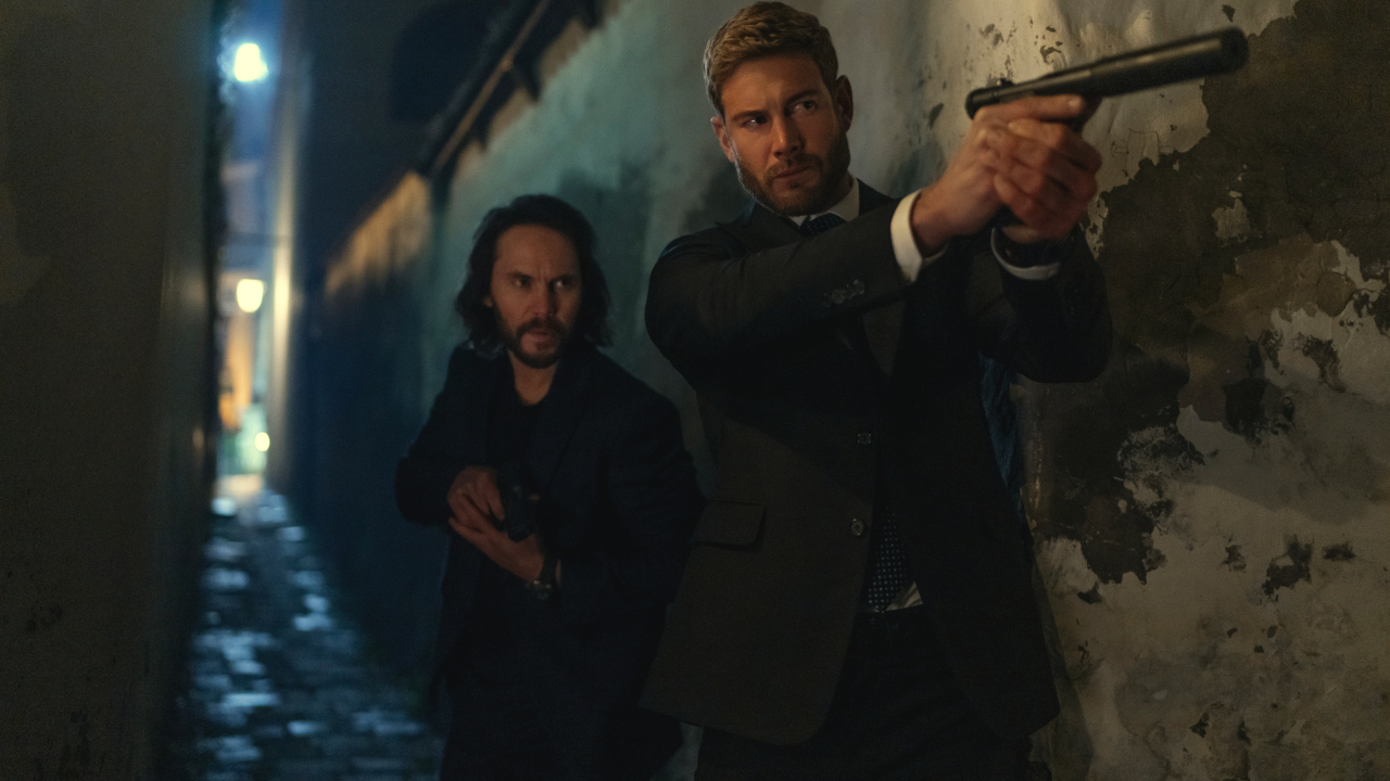Taylor Kitsch crouches behind Tom Hopper during a shootout in The Terminal List: Dark Wolf.