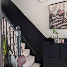 Staircase with half black, half white wall with framed artwork, and neutral carpet going up stairs