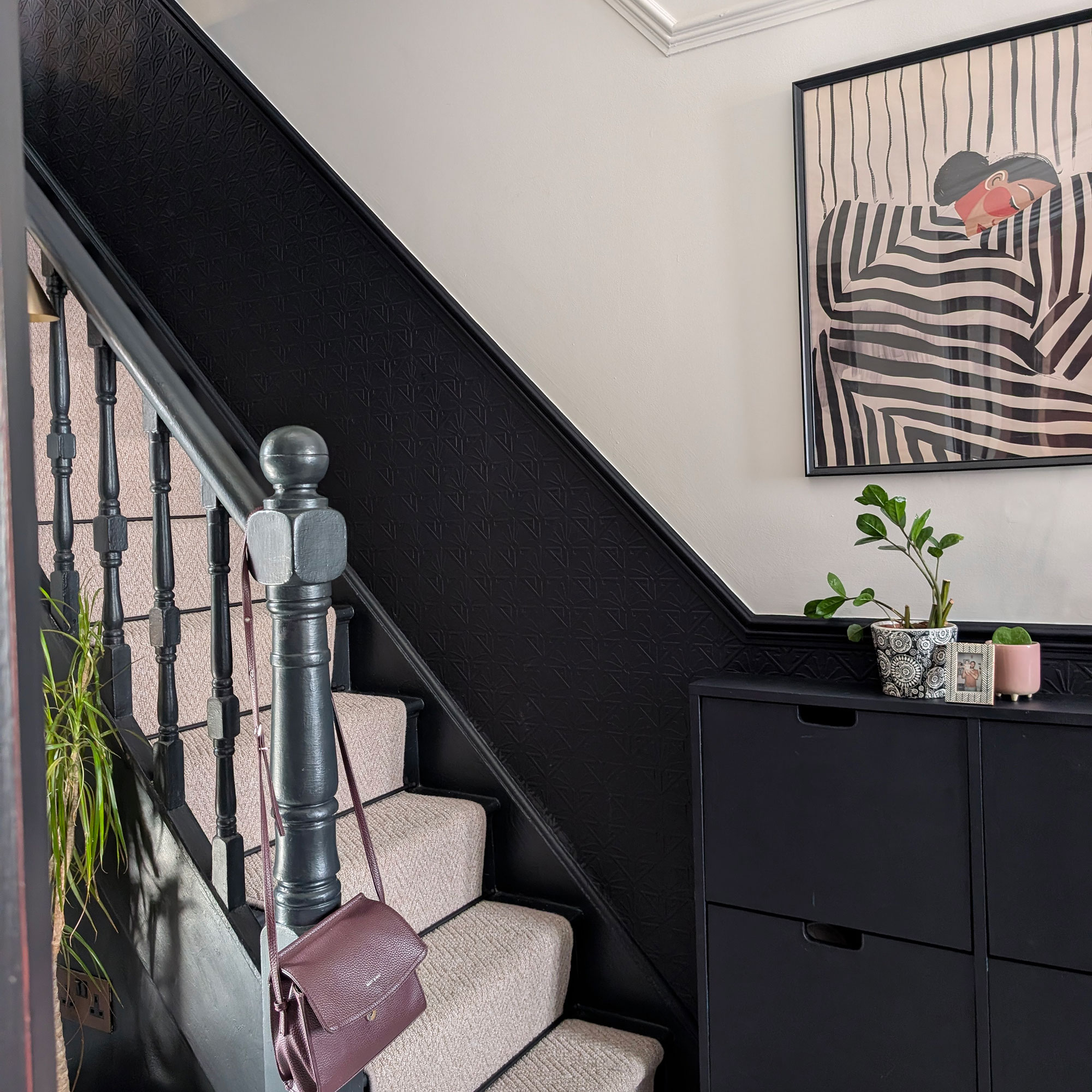 Staircase with half black, half white wall with framed artwork, and neutral carpet going up stairs