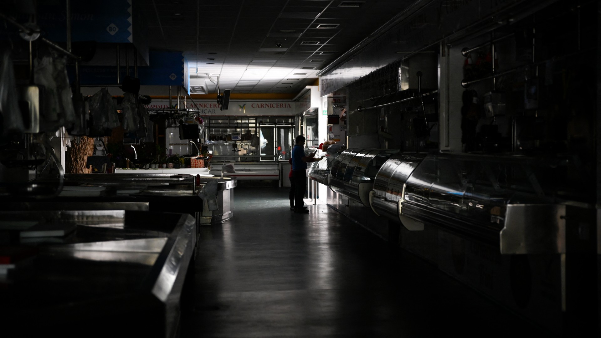 a lone person stands silhouetted by the light of an open door in a dark supermarket