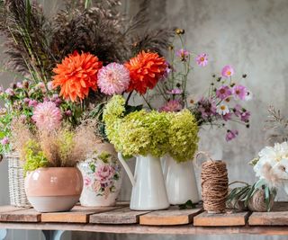 Mixed bouquets on flowers in a variety of jugs and vessels displayed on a wooden workbench