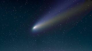 A photograph of a bright white comet with a trail streaking behind in the starry night sky