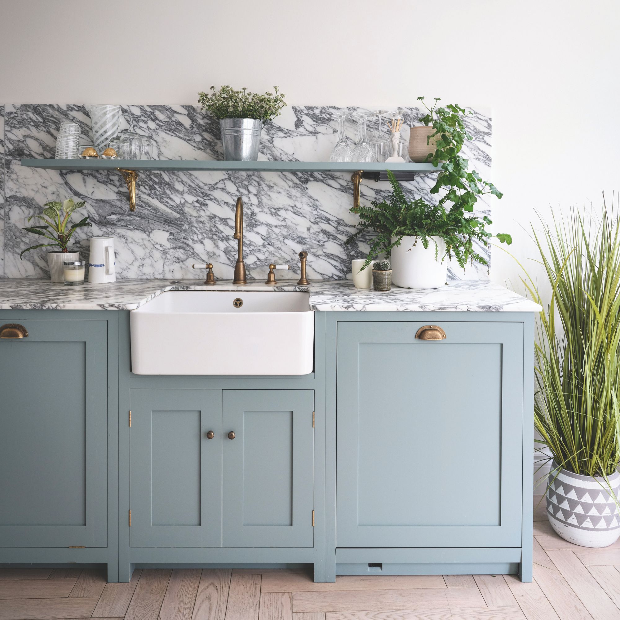 Kitchen area with blue cabinets, a marble worktop and splashback, and white sink, with a plant to the right 