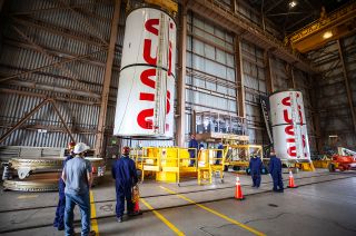 NASA Exploration Ground Systems and Jacobs workers watch as one of the two "worm"-emblazoned solid rocket booster segments is moved into place inside the Rotation, Processing and Surge Facility at Kennedy Space Center in Florida.