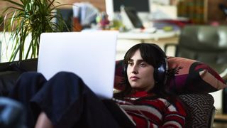 A girl wearing headphones lying back on a couch on her laptop