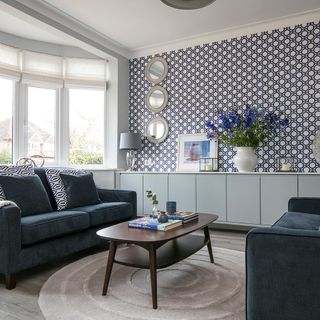 A pair of blue sofas arranged around a coffee table in a living room with white and blue circular patterned wallpaper.