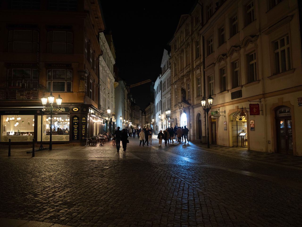 A street in Prague busy with people lit up at night by store windows