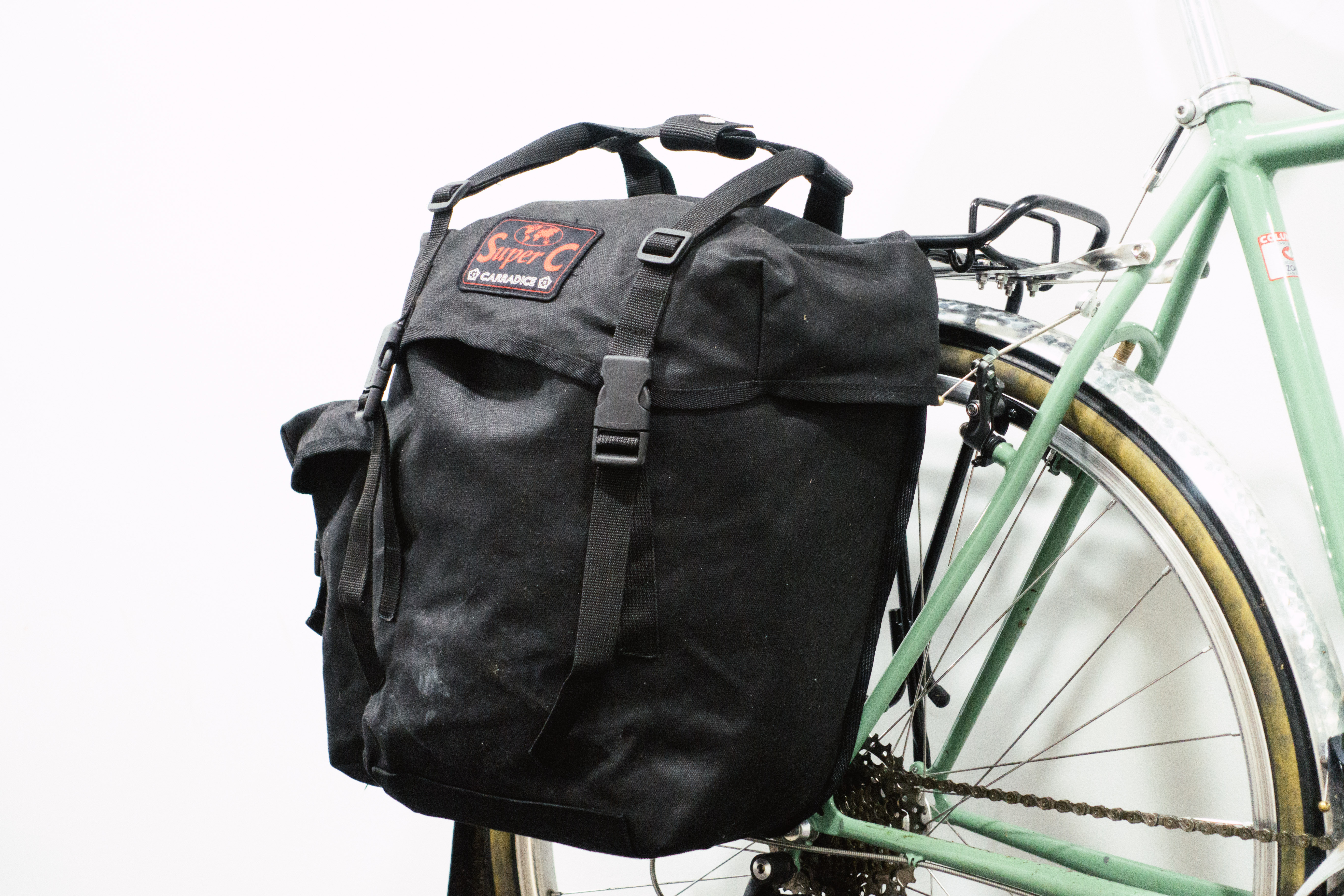 A black canvas pannier mounted to a green bike against a white background