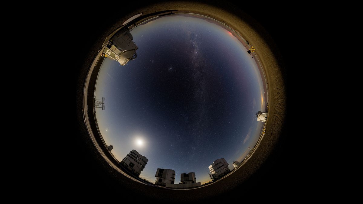 many bright dots can be seen in a starry night sky above a cluster of buildings in a desert