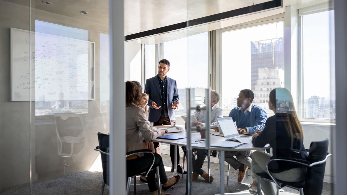 Staff meeting in an open plan office space with senior leader presenting to co-workers.