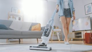 A vacuum cleaner being used on a rug next to a couch