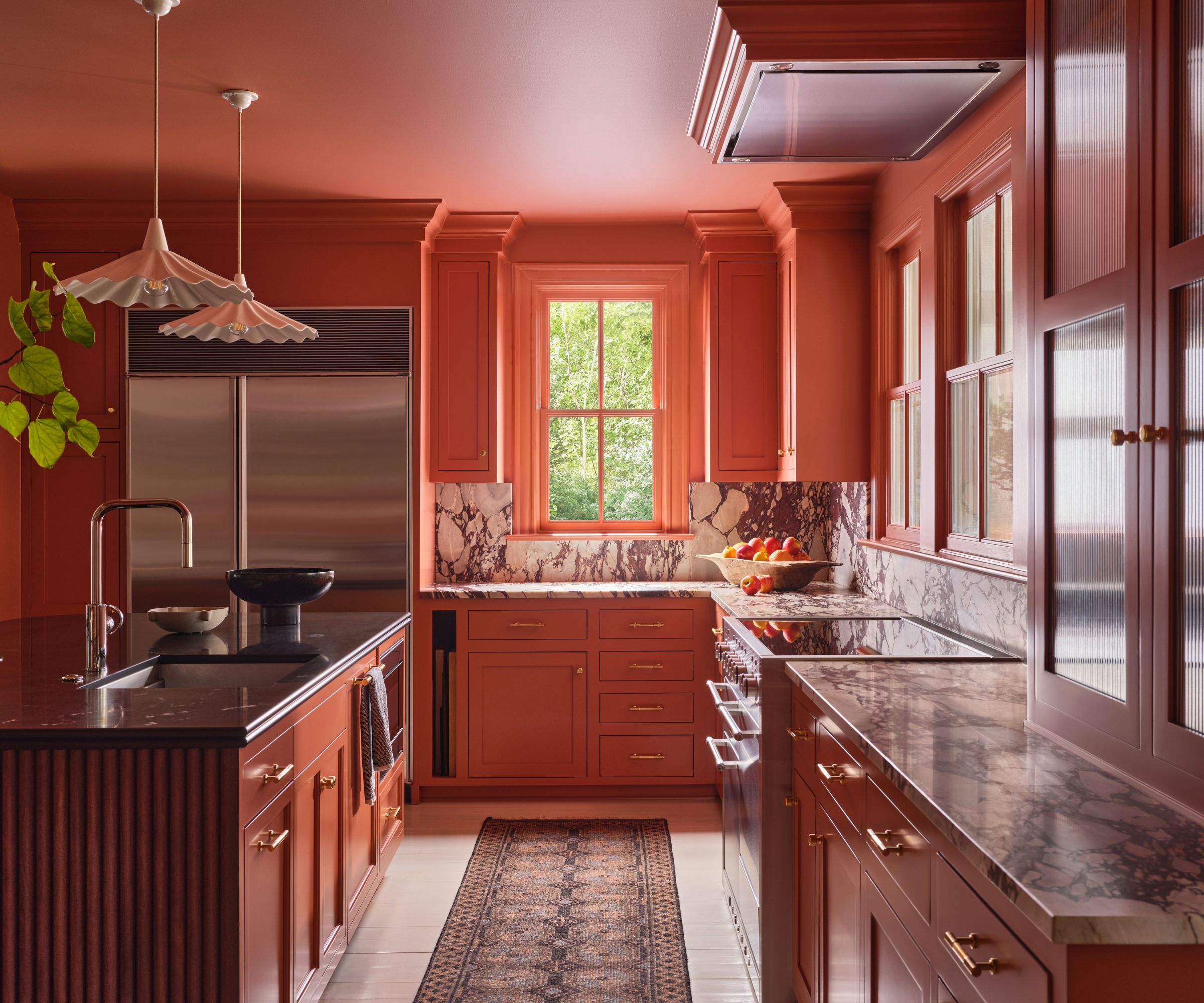 A color drenched terracotta kitchen with stainless steel appliances and a fluted wood island