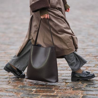 A close up shot of a woman walking down the street carrying a chic bacl work bag - 1975353224