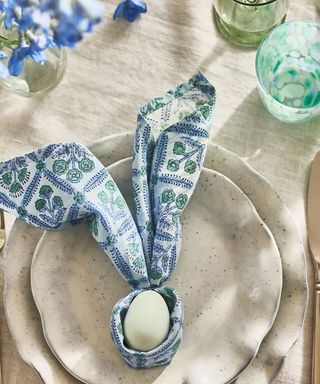 easter table laid for the anthropologie easter 2025 collection with a styled napkin shaped like bunny ears with an egg in the middle