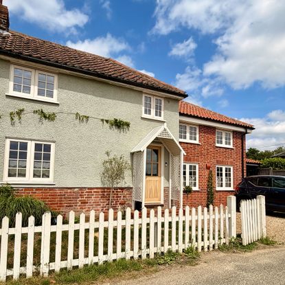 Pale green home with brick base, with cream porch and matching wooden fence