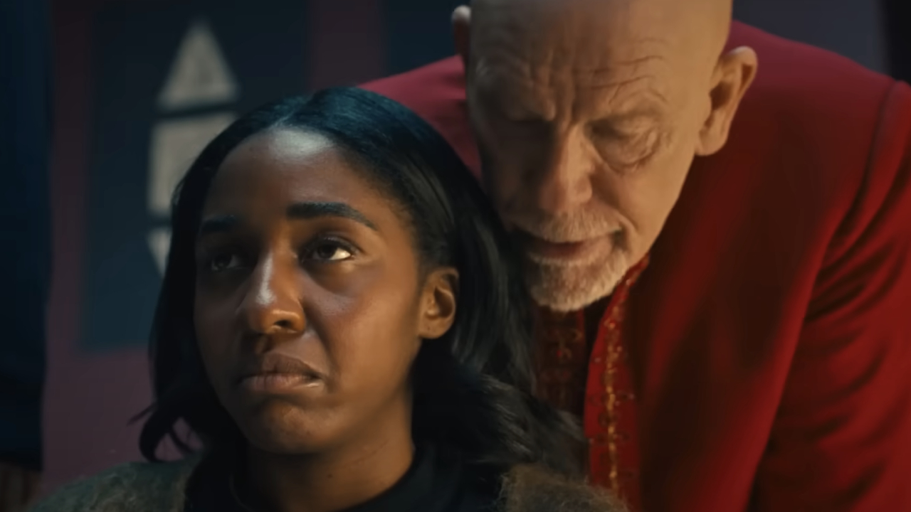 Ayo Edebiri looking uncomfortable as John Malkovich talks to her from behind in Opus