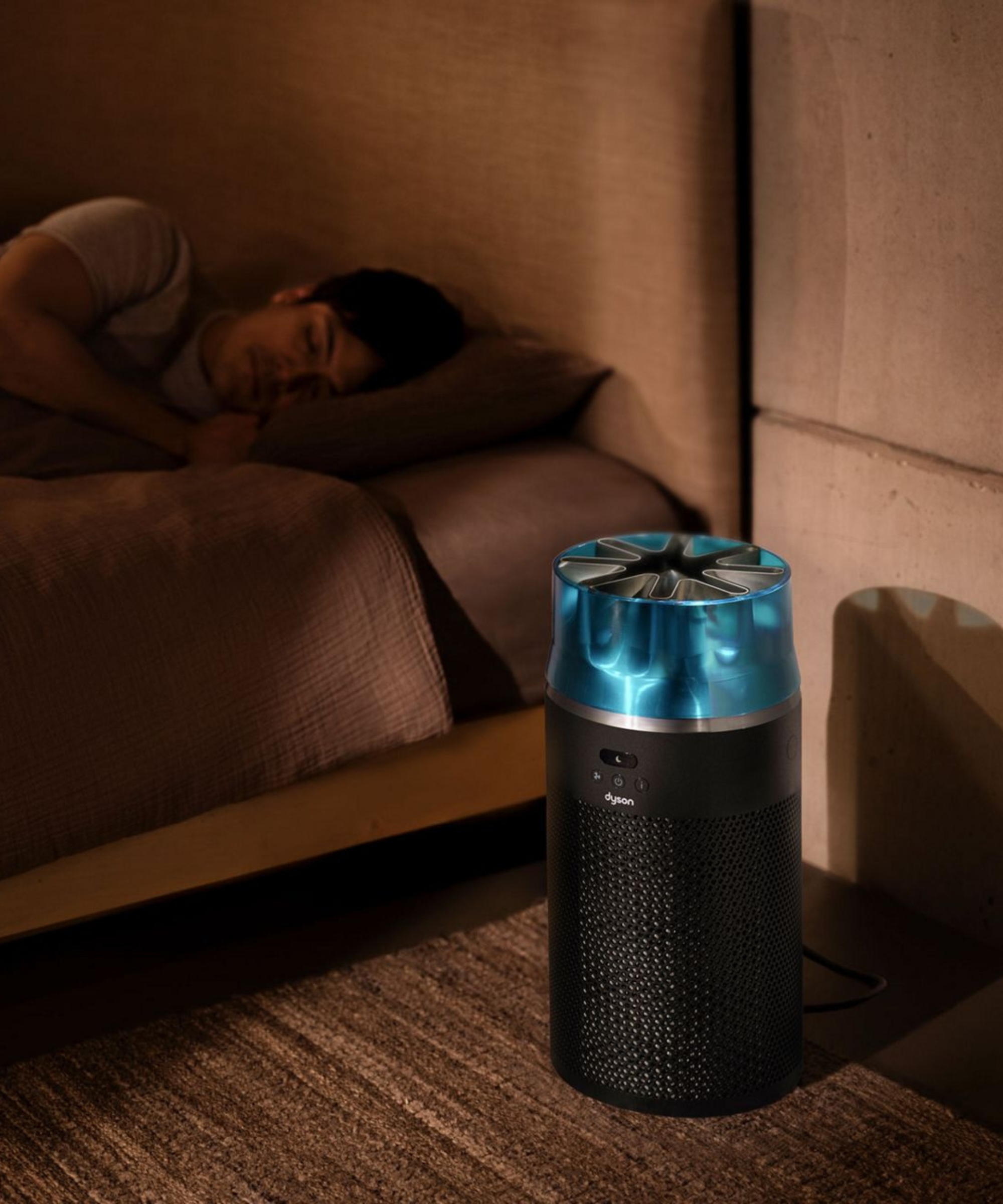 Dyson HushJet air purifier in dark, brown bedroom next to person pictured sleeping in bed.
