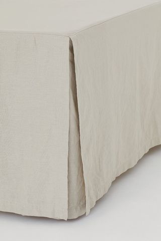 edge of a bed with linen bedskirt draped to the floor