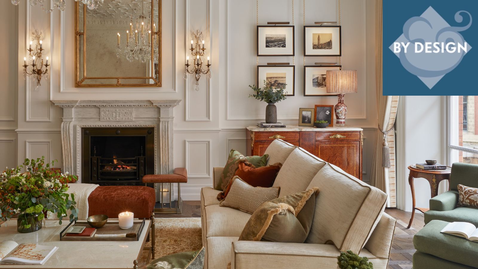 Luxurious living room with white panelled walls, artwork and wall lamps, cream sofa and coffee table in fron of fireplace, windows and green seating to the right