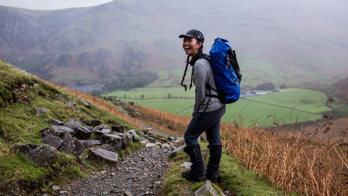 A woman standing on a hillside, wearing a SealLine Bigfork Dry Daypack on her back.