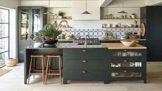 a green Kitchen by Cave Interiors with a green kitchen island, tiled backsplash, wooden floor, and a large green cabinet, and floating wooden shelves