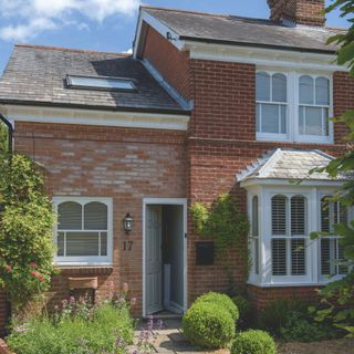 Exterior of a brick cottage-style house, with the grey front door open and a lush front garden