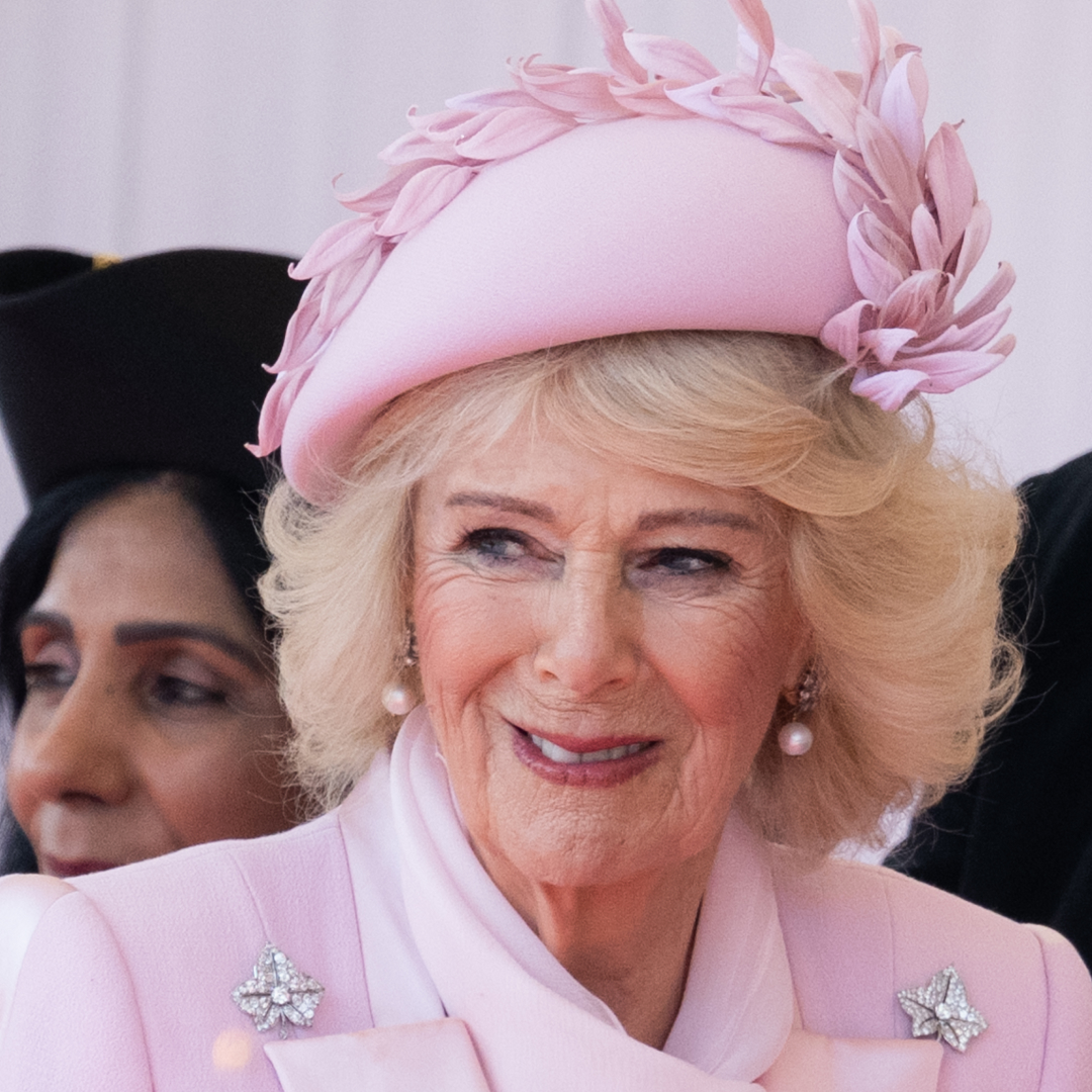 Queen Camilla in a pink hat and coat smiling