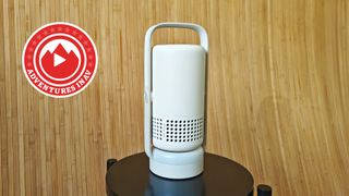 The Xgimi Vibe One projector on a black stool, with a wooden brown background.