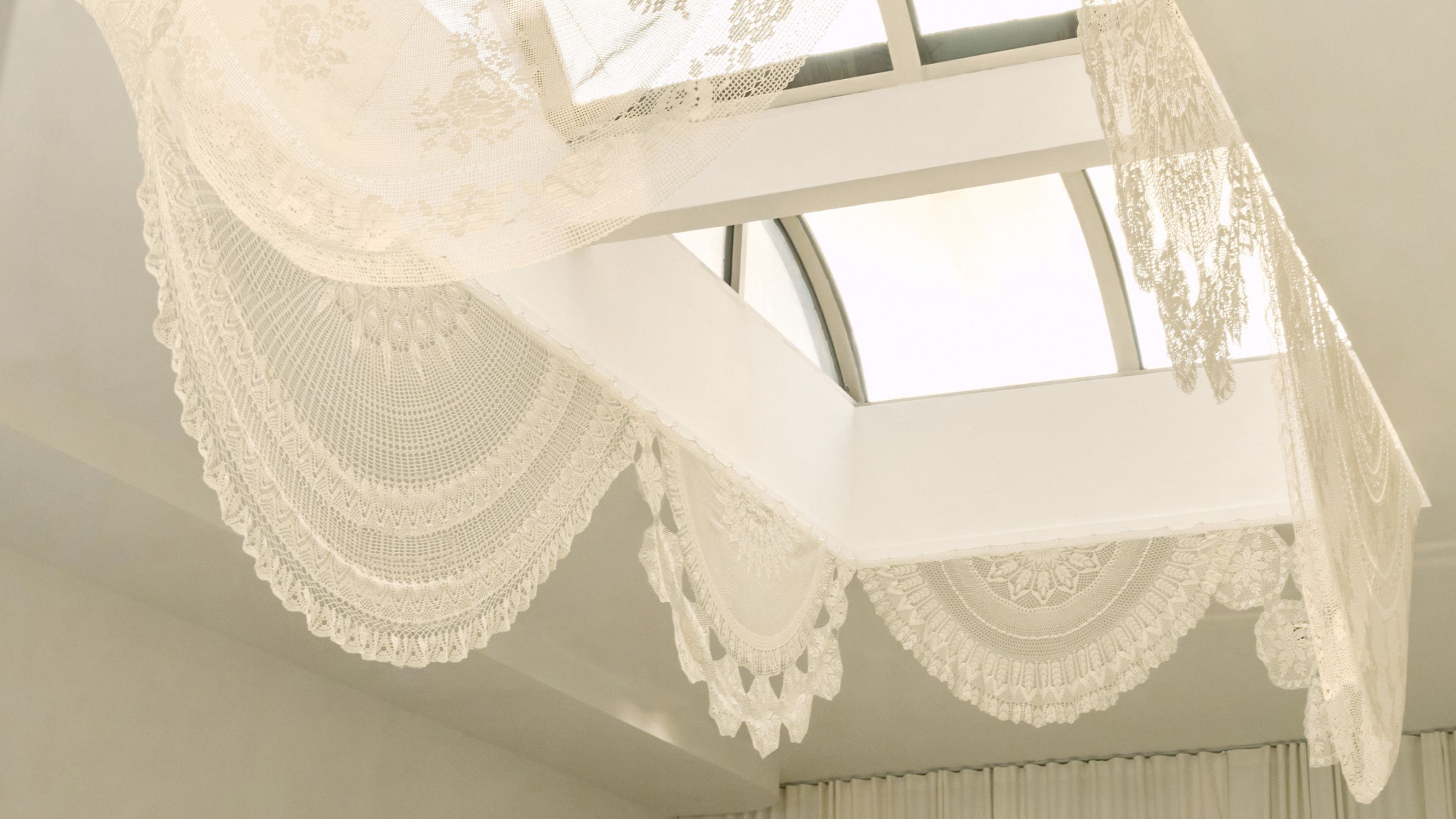 looking up to a skylight in an open double-height room with lace curtains draping down