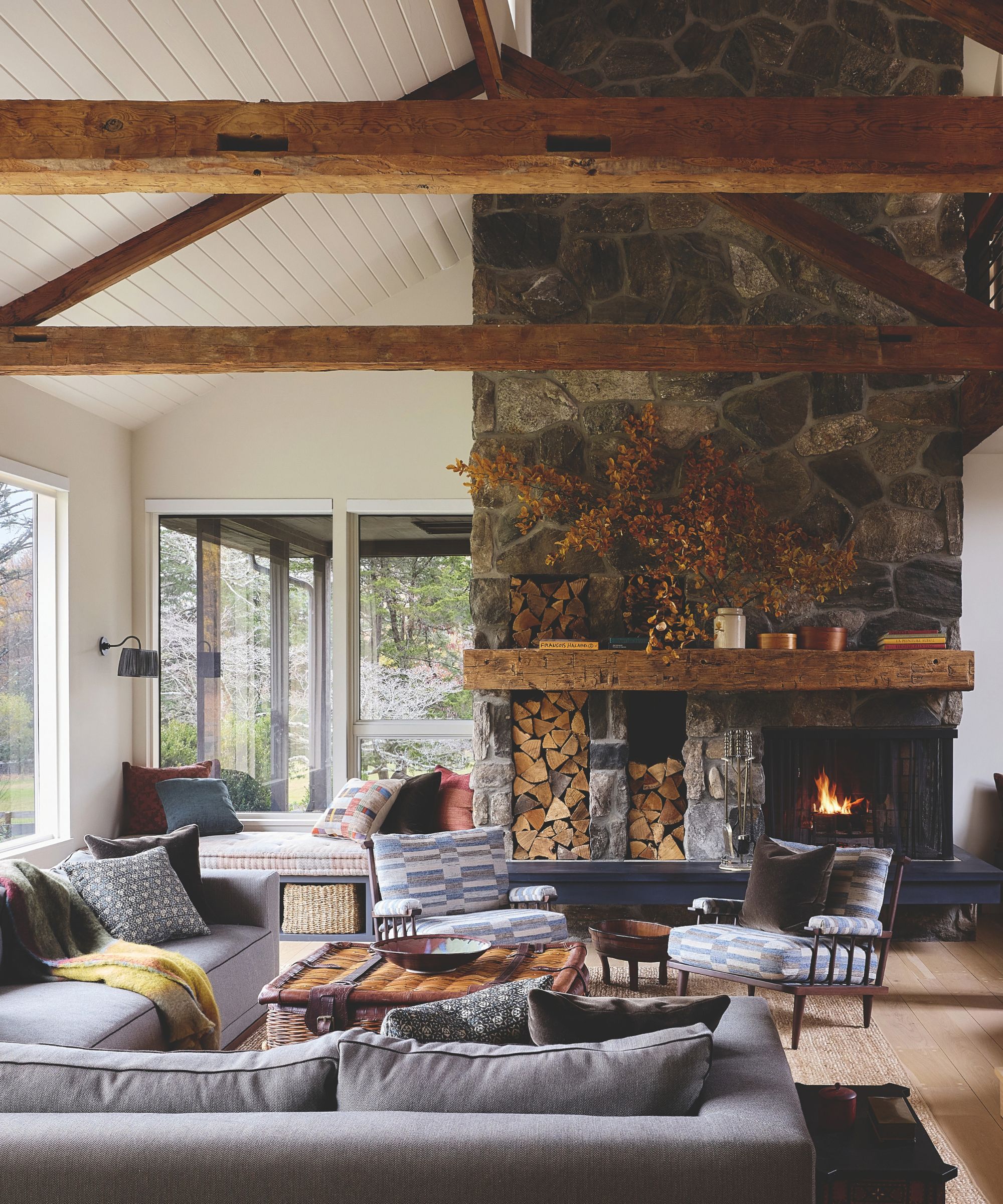 Cozy living room featuring high vaulted ceilings with timber beams, floor-to-ceiling stone fireplace, and comfortable gray seating.