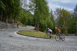 Two road cyclists rounding a cobbled hairpin bend on a Slovenian road