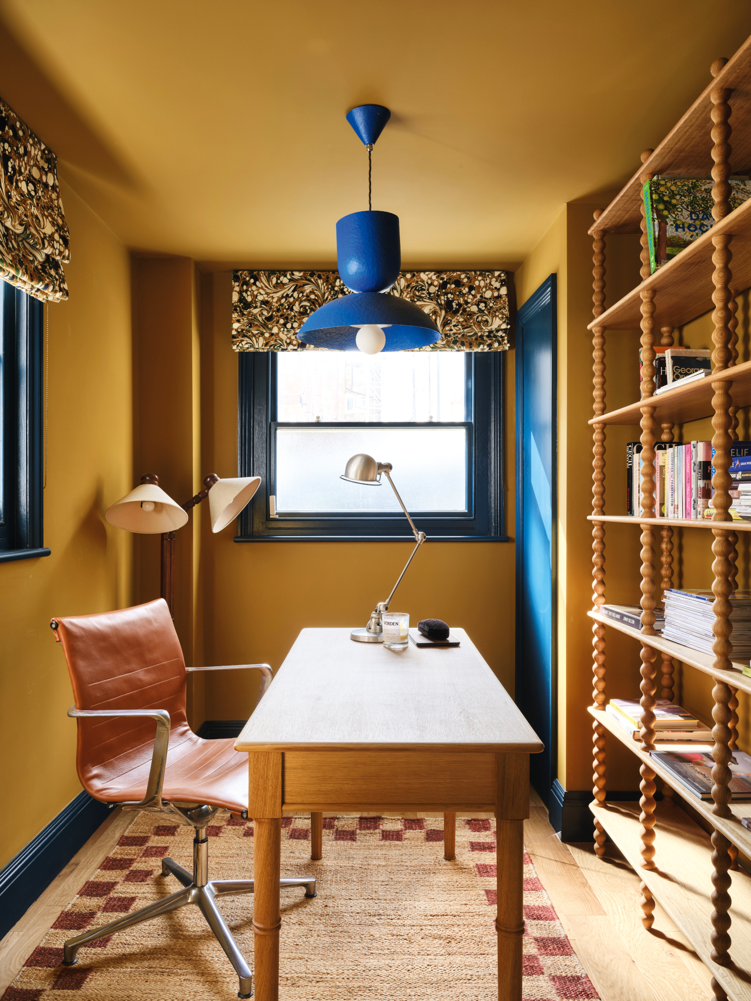 Yellow home office with ochre walls, oak shelving and desk, tan desk chair and cobalt blue pendant light