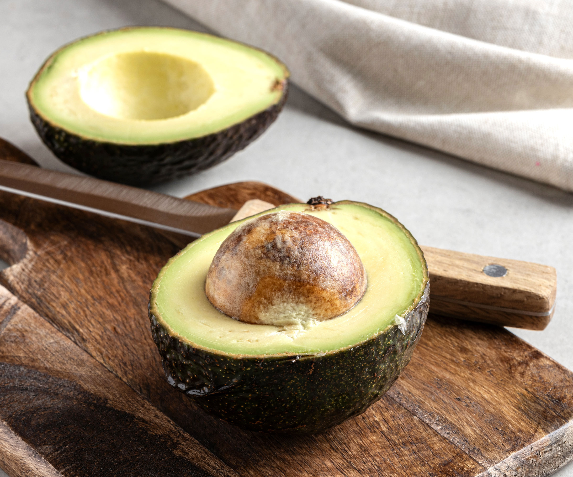 avocado fruit sliced in two showing pit with chopping board and knife