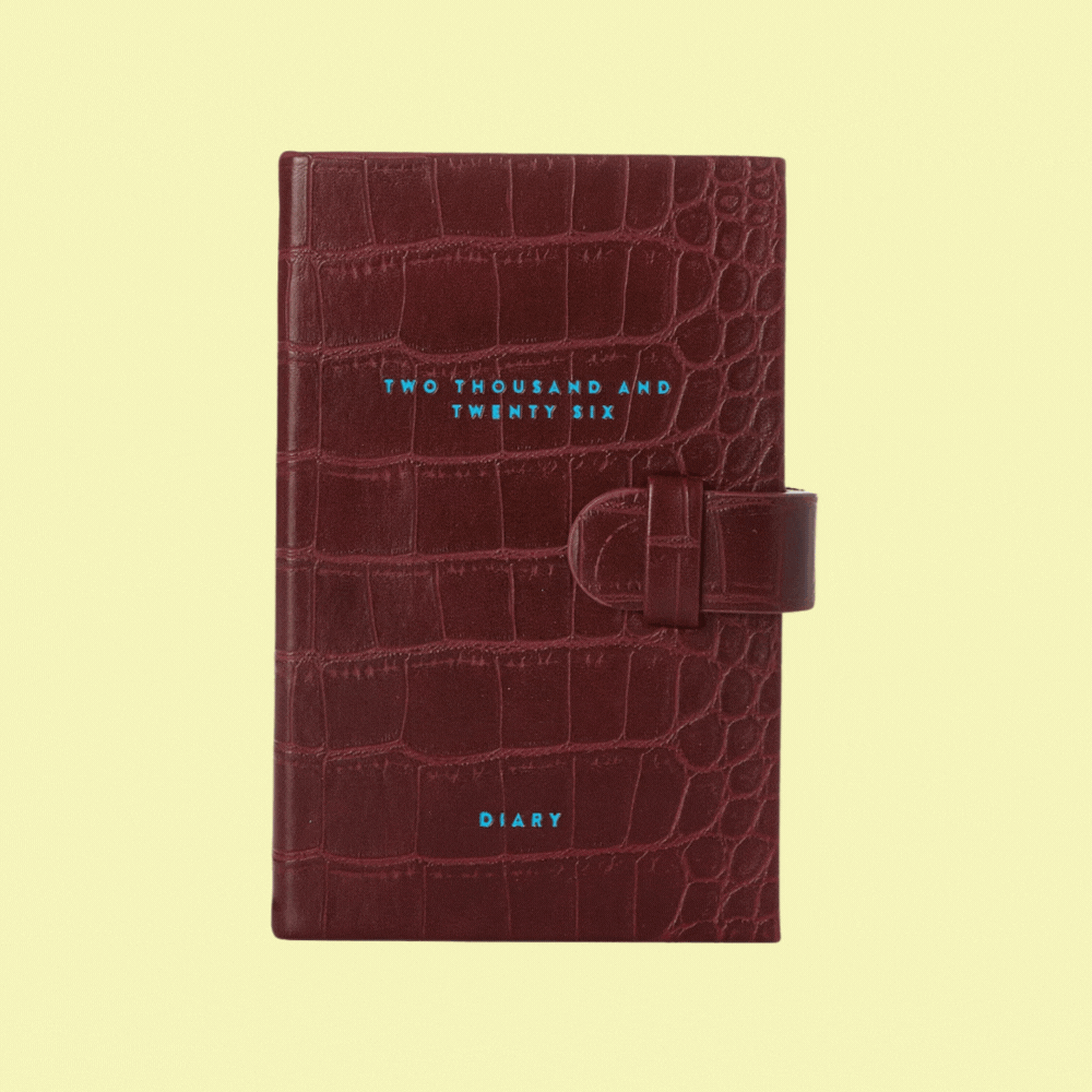 ScribbleandDotCo Burgundy Pocket Diary 2026 - 2027 Diary With Monthly Tabs against pale yellow background, shown in a rotating gif as both open and closed.