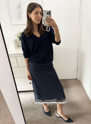 Woman in navy sweater and polka-dot skirt.