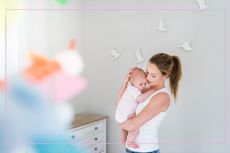 A woman carrying a baby in a nursery room with birds on the wall