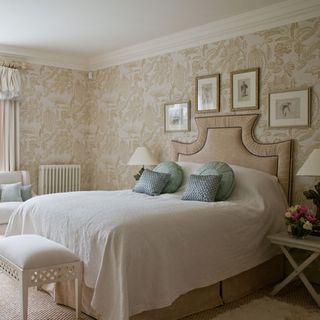 Guest bedroom with pale patterned-wallpaper and antique framed prints