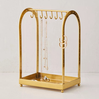 A gold jewelry stand with arches, necklace hooks, and holes for earrings