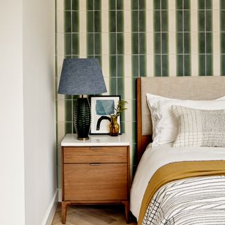 A luxury bedroom with cream and green arch tile decor, bed, denim blue lampshade, wood and white bedside table and black framed art