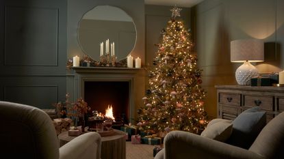 A large christmas tree in a cozily lit living room with a roaring fireplace