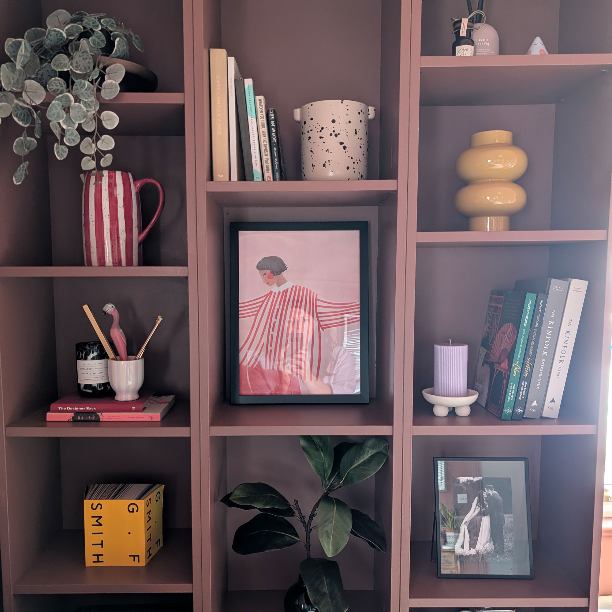 Dusky pink painted bookcases styled with art, vases, books and plants